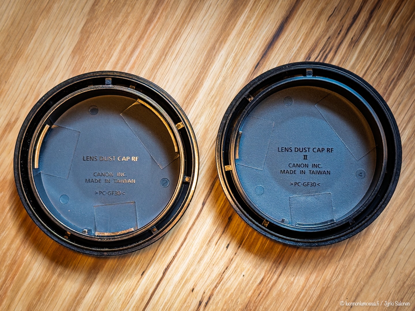 Kaksi Canon-objektiivin pölysuojaa puulattialla; molemmissa teksti "Lens Dust Cap RF, Made in Taiwan".